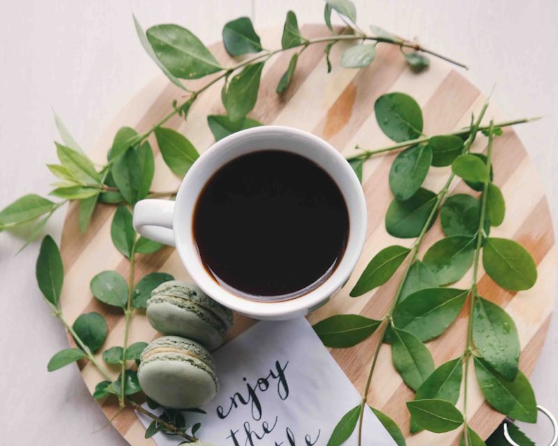 flat lay photography of leaves with cup of coffee and three macarons on chopping board